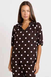 Front view of the Betty Basics Joanne Blouse in chocolate with pink polka dots, showing a gathered V-neckline and short puff sleeves.