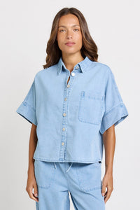 Model wearing Betty Basics Dawn Denim Shirt in medium wash with a relaxed, boxy fit and oversized short sleeves close up front view