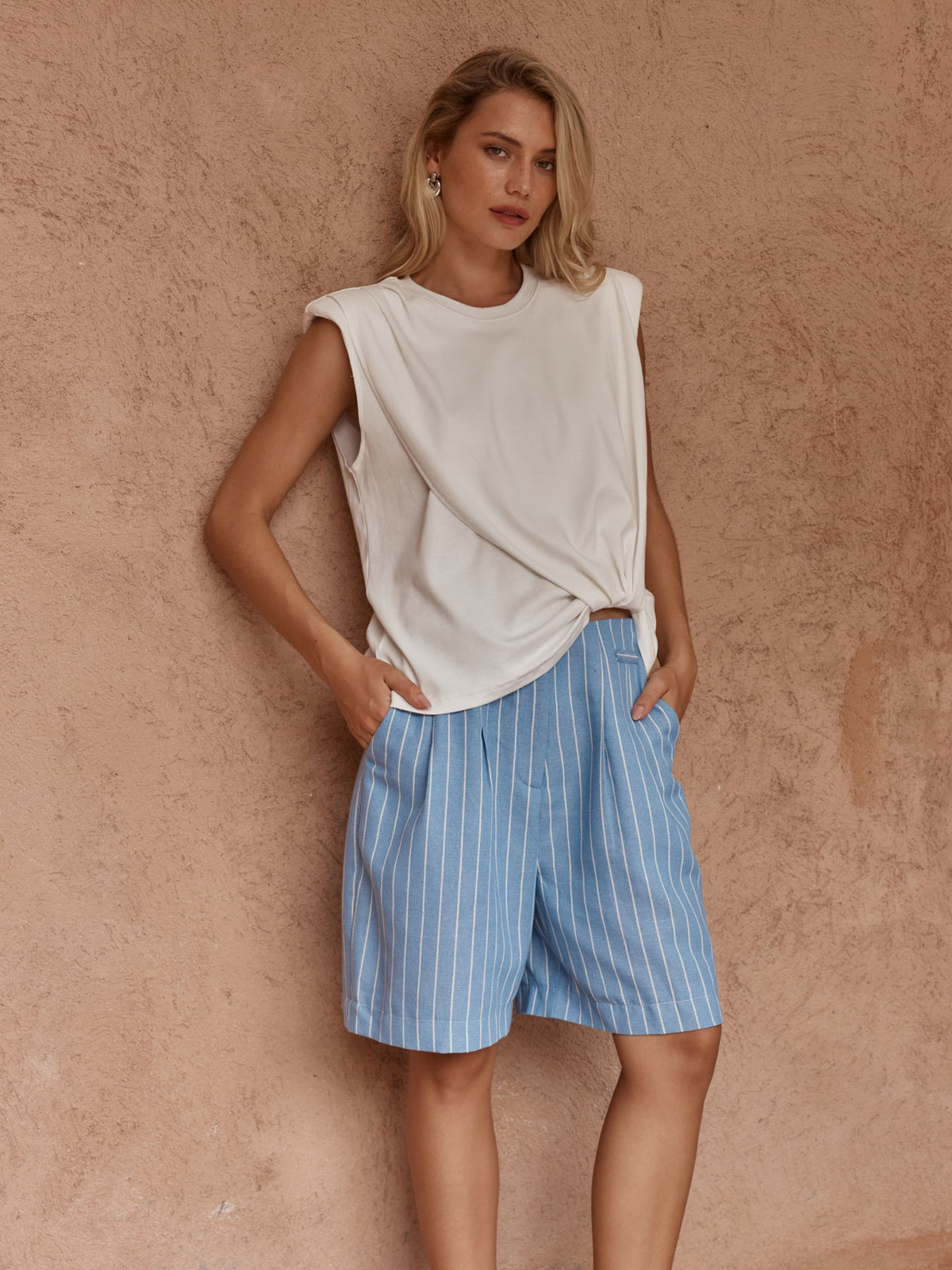 Model wearing the Sass Marley Knot Front Tank in white with blue striped shorts, showing its crew neckline and draped front hem.
