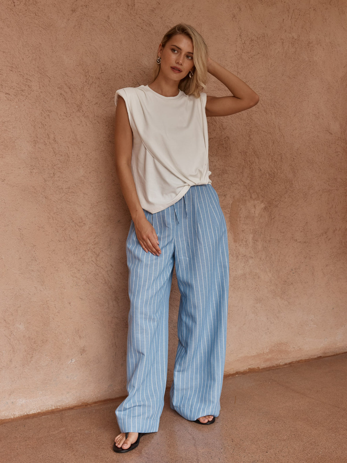 Model wearing the Sass Marley white knot-front tank with blue striped wide-leg pants and sandals.