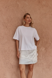 Front view of a model wearing the Sass Arlo Jersey Lace Tee in Ivory with an asymmetrical satin lace hem, crew neckline and short sleeves