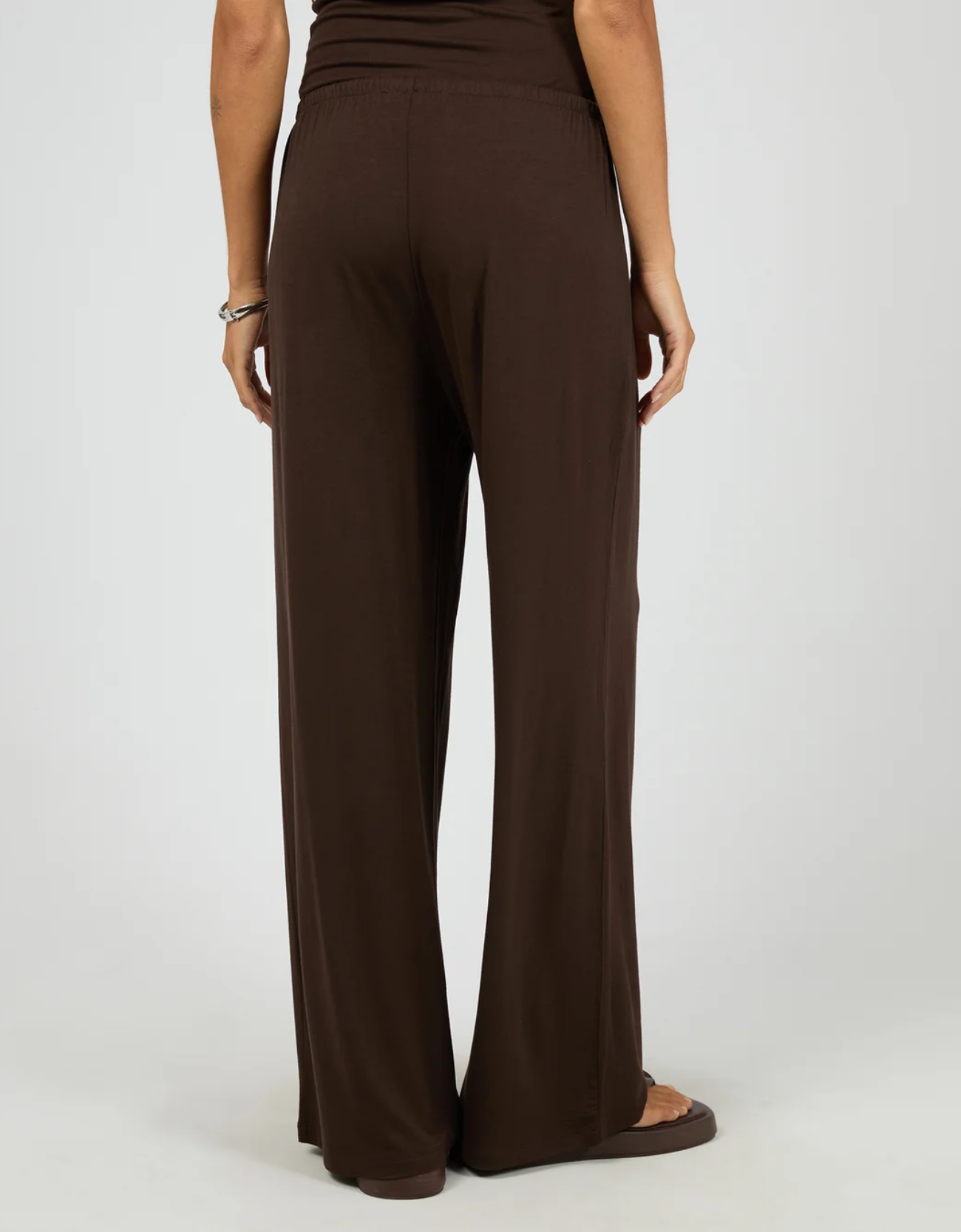 Silent Theory Dara Pant in Chocolate – back view showing clean wide-leg silhouette, elasticated waistband and full-length hem in soft chocolate stretch viscose, styled with brown platform sandals