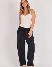 Model wearing the black One Ten Willow relaxed pull-on pant with a cream camisole, against a light grey studio background.