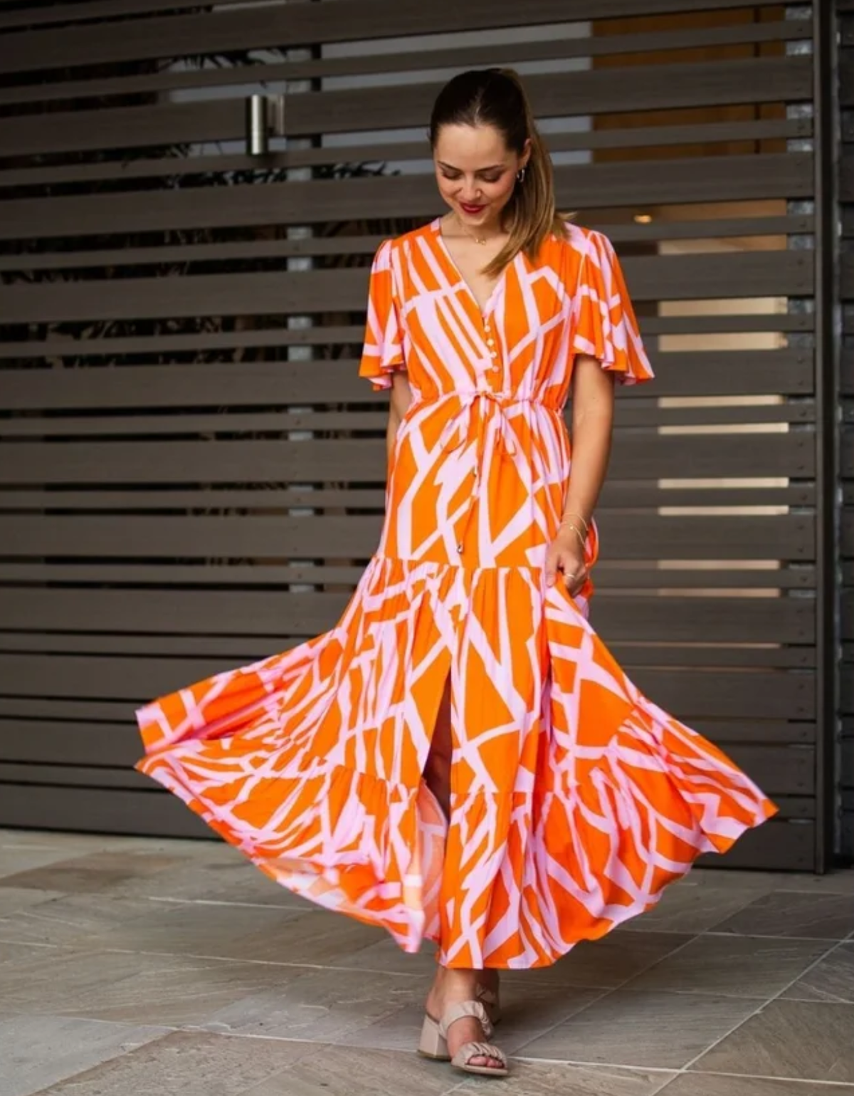 Fria The Label Selma Maxi Dress in orange and soft pink geometric print, showing flutter sleeves, a drawstring waist and flowing tiered skirt.

