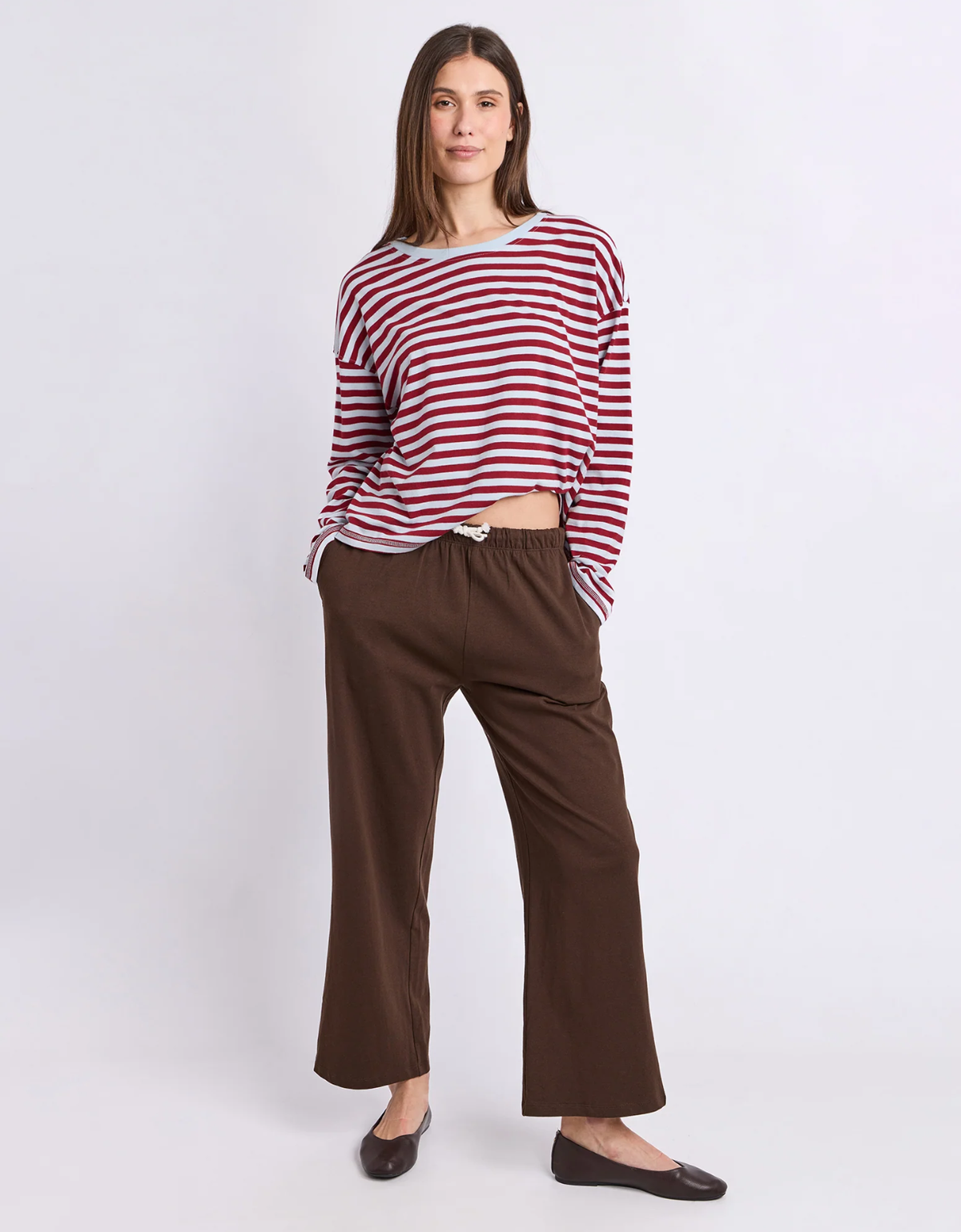 Full length view of a model wearing the Foxwood Lola Stripe Long Sleeve in Burgundy & Light Blue with brown trousers and brown flats.

