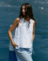 Sass Elin white cotton top worn beside the water, showing adjustable side ties and gathered rows through the body.