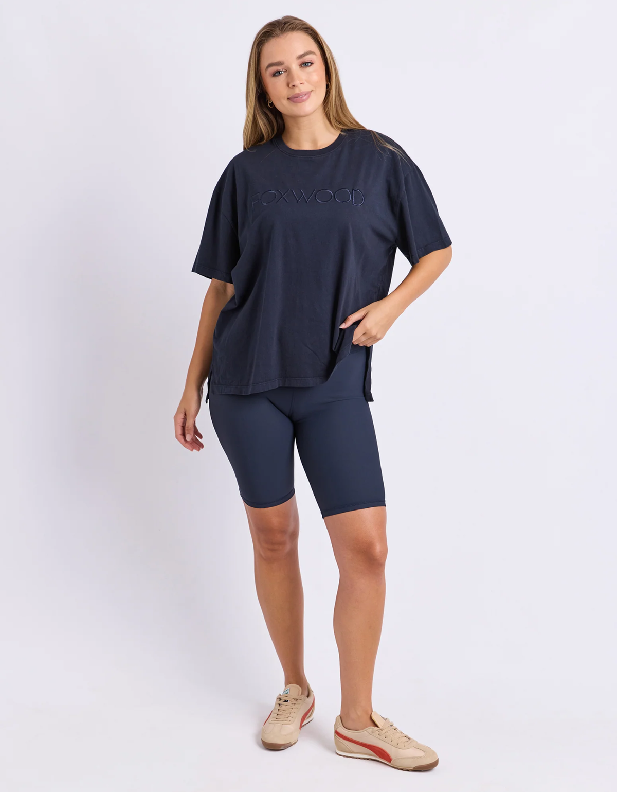 Front view of the navy Foxwood Simplified Tee worn loose over navy bike shorts with sneakers, showing its relaxed fit and side splits.