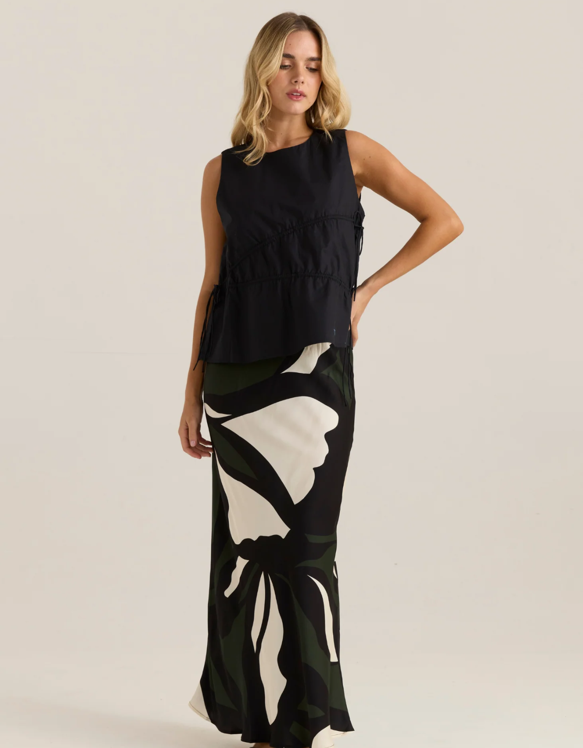 Model wearing the Sass Elin black gathered tie top with a black, cream and green printed maxi skirt.
