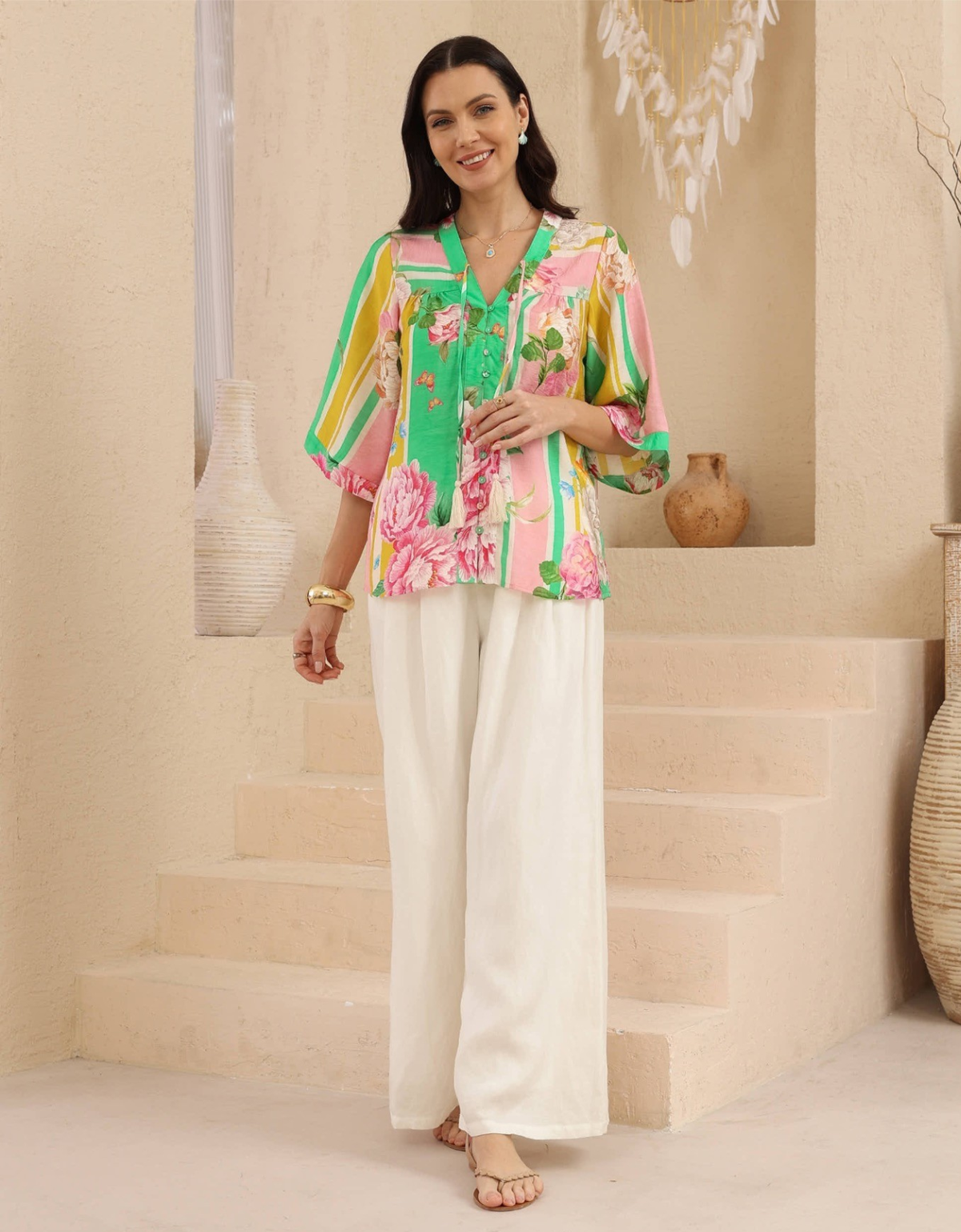 Model wearing the Iris Maxi Janet green floral stripe blouse with white trousers, showing its relaxed fit and flowing sleeves.