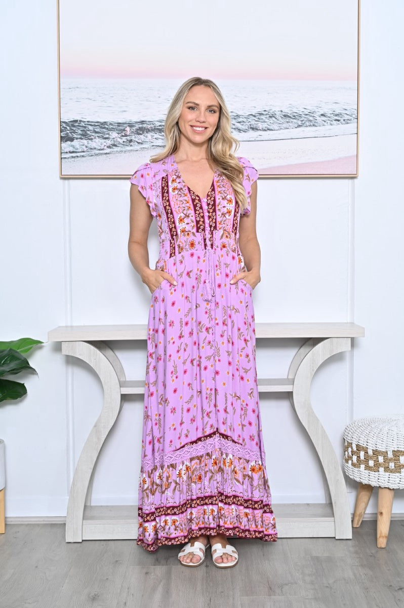 Model wearing the New U Collection Posy Maxi Dress in pink floral print, showing burgundy borders, flutter sleeves, a drawstring waist and side pockets.